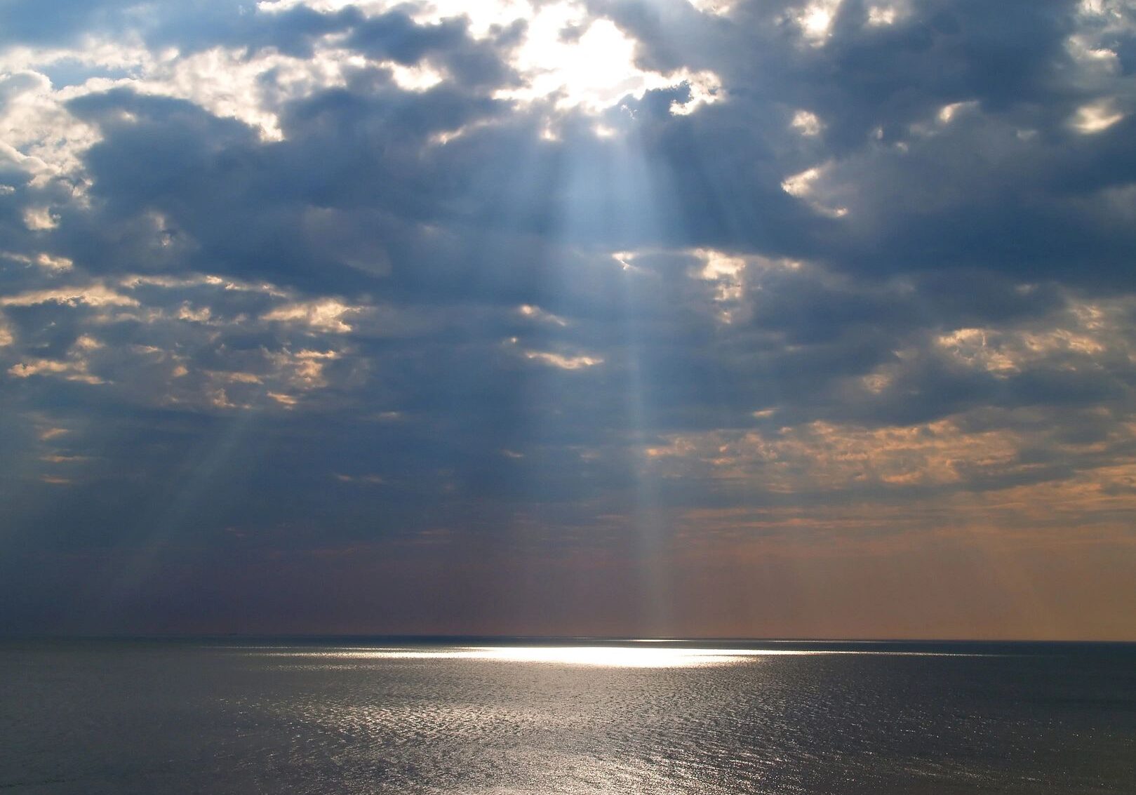 Sunbeams breaking through clouds over calm sea